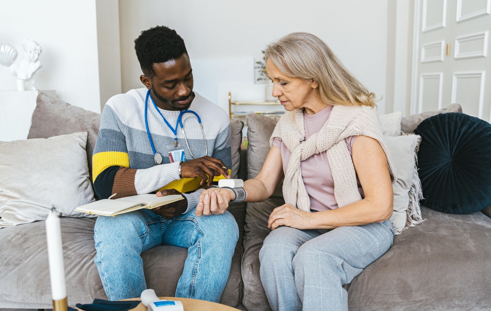 Healthcare professional checking blood pressure of elderly woman in a cozy indoor setting.